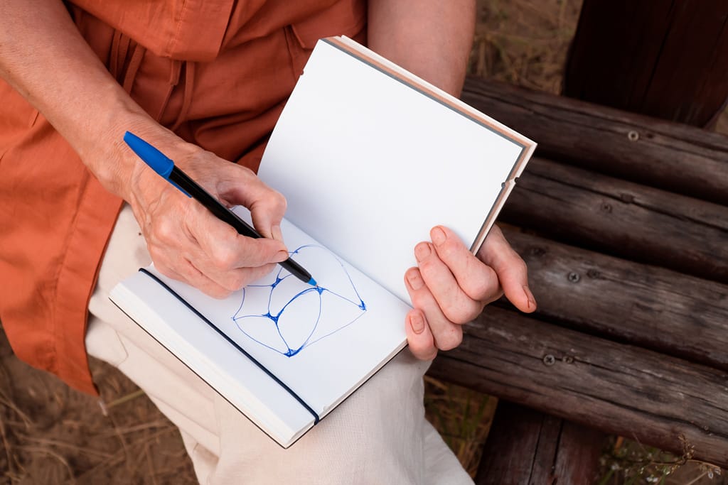 Close-up of female hands drawing express neurographic art in notebook outdoors. Abstract neurographic drawing with only pen