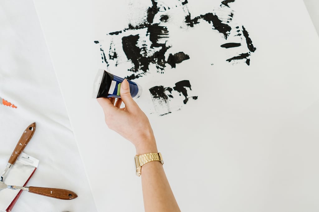 Woman's hand drawing on white canvas using black oil colors. Many drawing instruments near on the floor.