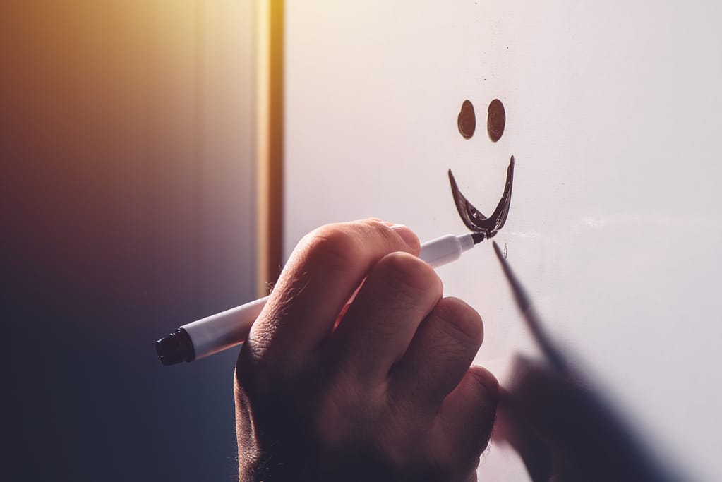 Male hand drawing smiley emoticon on office whiteboard, happy satisfied businessman during business results presentation, selective focus
